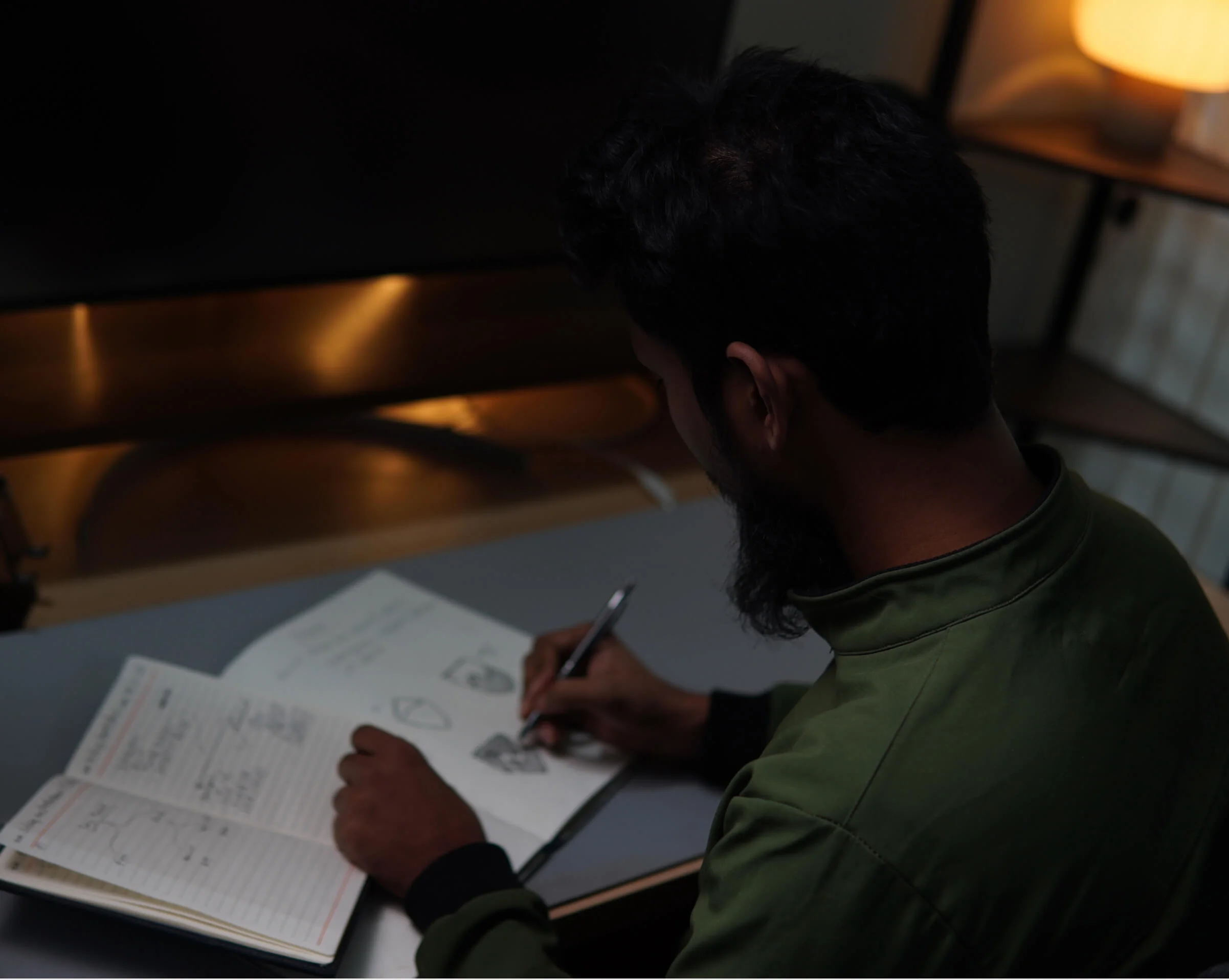 A Panze designer sketching logo ideas in a notebook at a desk lit by a warm lamp